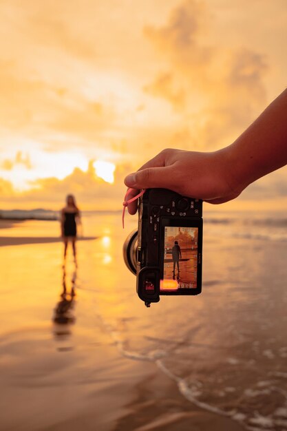 Foto een camera met handen fotografeert een balinese vrouw die een gymnastische beweging doet op een zwart shirt vlakbij het strand