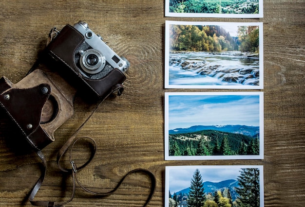 Een camera op houten planken. De oude camera ligt op een houten ondergrond in de buurt van foto's met een landschap. Uitzicht van boven