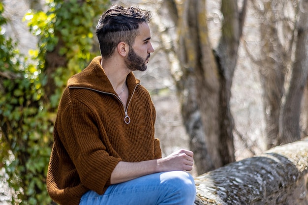 Een casual man met een bruine trui en een zonnebril die wegkijkt terwijl hij op een steen zit