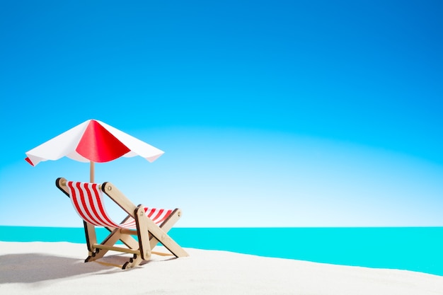 Een chaise longue onder een parasol op het zandstrand aan zee en lucht met kopie ruimte