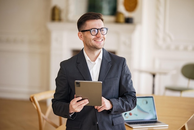 Een charismatische zakenman met een aantrekkelijke glimlach navigeert vakkundig op een tablet zijn elegante pak