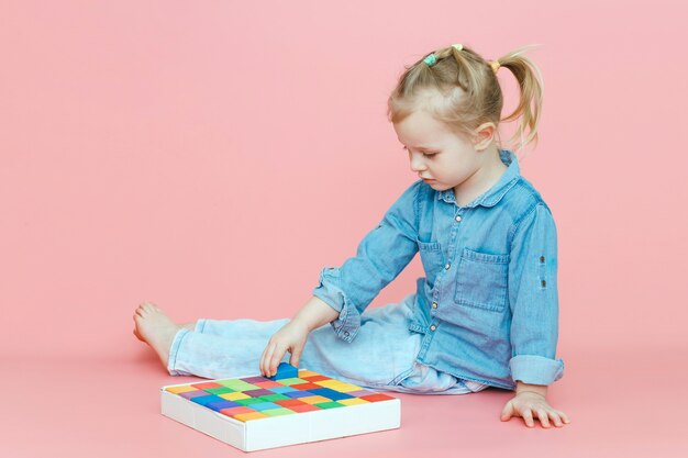 Een charmant klein meisje in denimkleren op roze