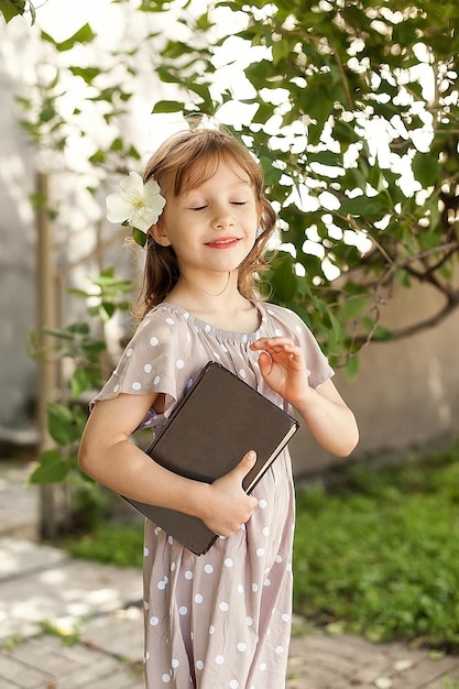 Een charmant klein meisje in een zomerpark met haar ogen dicht en een boek in haar handen Het concept van een gelukkig leven