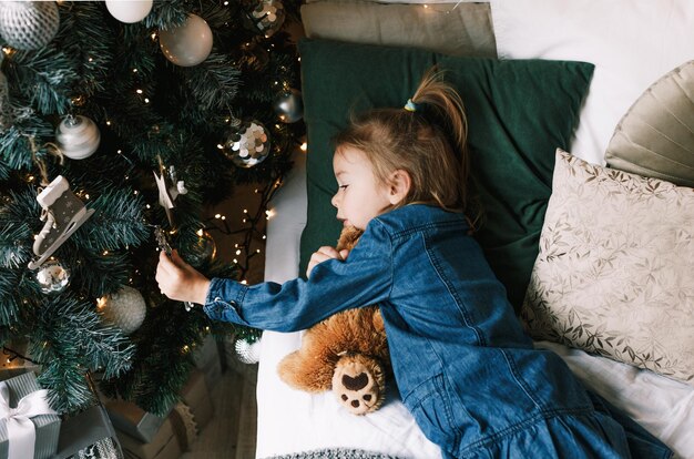 Een charmant meisje slaapt met haar teddybeer onder de kerstboom