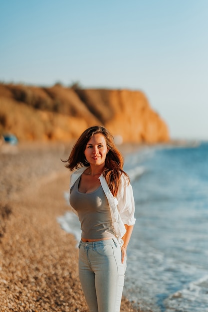 Een charmante jonge vrouw in een wit overhemd en een spijkerbroek op een rustig romantisch strand aan zee