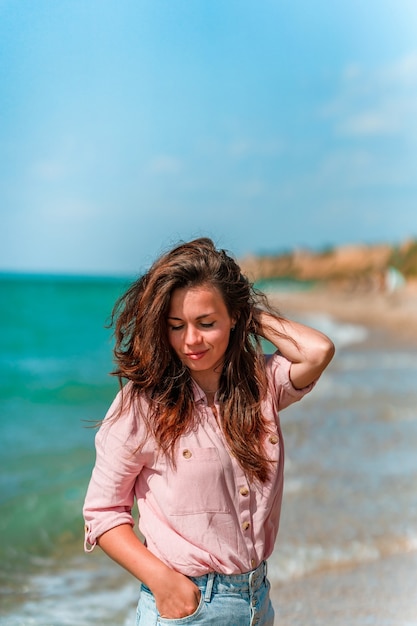 Een charmante jonge vrouw met lang haar en gekleed in een shirt loopt op een zonnige dag langs het strand