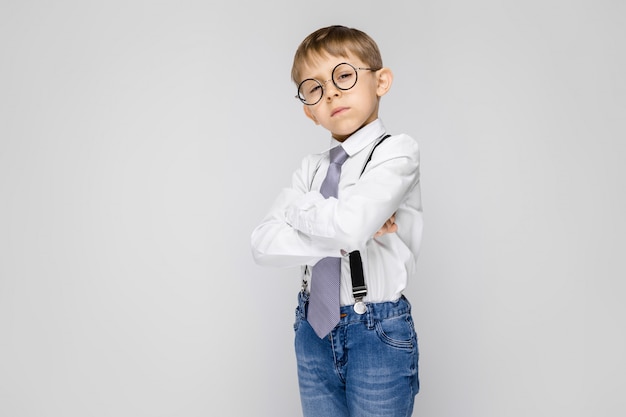 Een charmante jongen in een wit shirt, bretels, een stropdas en een lichte jeans