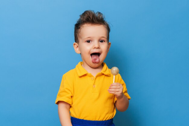 Een charmante jongen kijkt naar de camera terwijl hij een lolly op een blauwe achtergrond vasthoudt