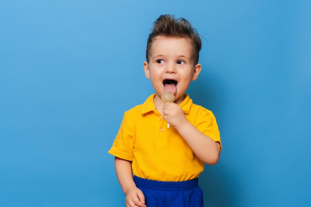 Een charmante jongen kijkt naar de camera terwijl hij een lolly vasthoudt op een blauwe achtergrond. Preventie van kindercariës