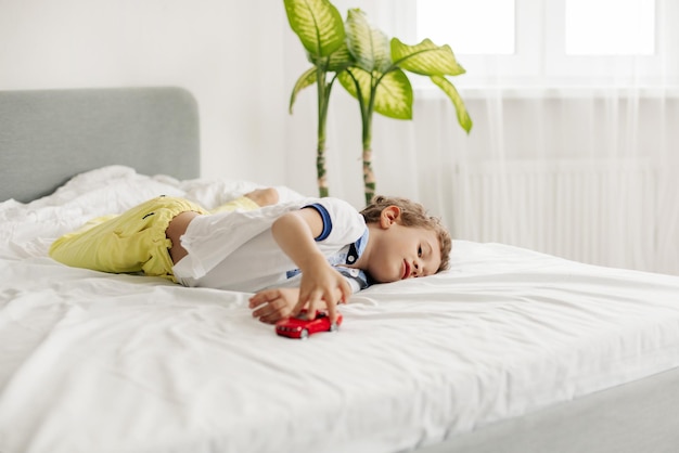 Een charmante jongen speelt met een speelgoedwagen op zijn bed.