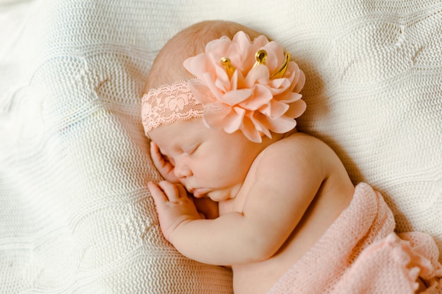Een charmante pasgeboren baby, gehuld in een zachtroze deken, slaapt op een gebreide plaid. Close-up portret.