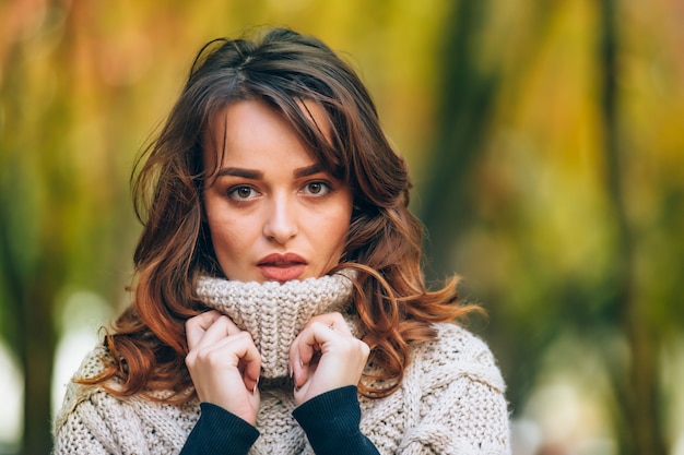 Een charmante vrouw met make-up raakt de gebreide kraag aan haar handen en kijkt recht in de camera o