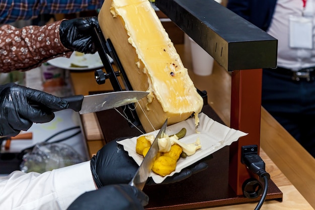 Een chef-kok bereidt een gerecht met raclette met behulp van een speciaal instrument voor het smelten van kaas.