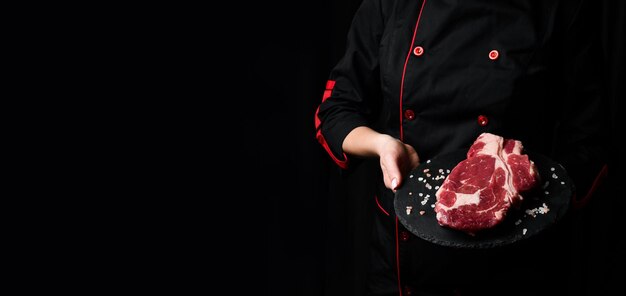 Een chef-kok bereidt ribeye rundvlees steak verouderde en gerijpte steak vlees op een zwarte achtergrond