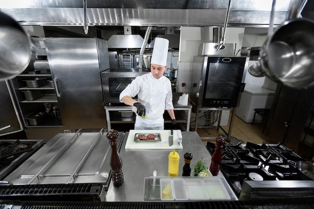 Een chef-kok in een wit uniform en een pet marineert vlees giet olie in een professionele keuken