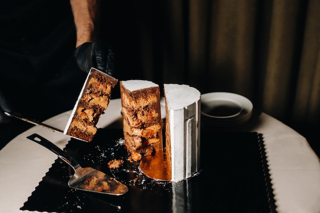 Een chef-kok met zwarte handschoenen snijdt een chocoladebruidstaart