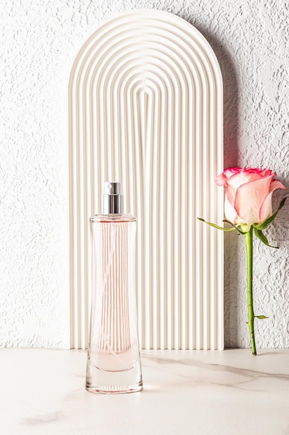 Een chique hoge fles damesparfum tegen de achtergrond van een witte decoratieve boog met een roze bloem Verticale weergave lege fles