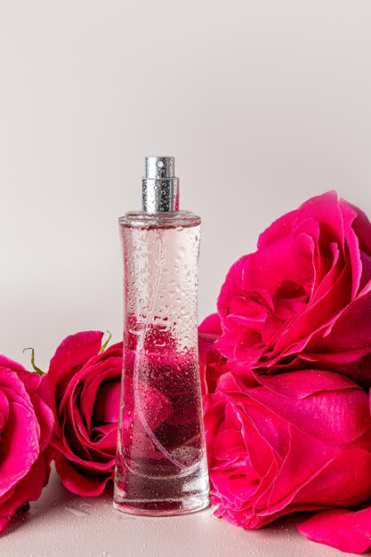 Een chique hoge fles parfum voor vrouwen op een pastel achtergrond met drie thee rozen Verticaal uitzicht Presentatie van de delicate geur van parfum