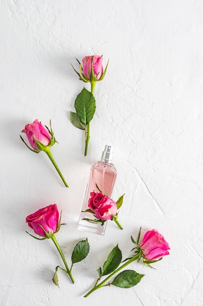 Een chique transparante fles cosmetica of spray op een witte achtergrond tussen verse rozen Vlakke verticale lay-outruimte voor tekst