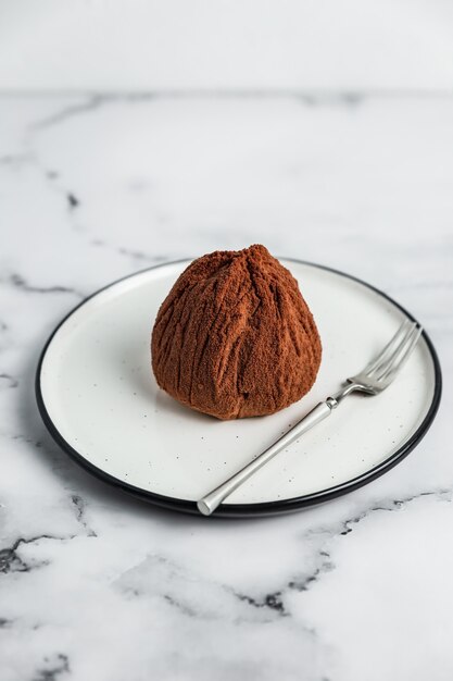 Een chocolademousse-dessert op een witte plaat, een vork, licht en helder marmer