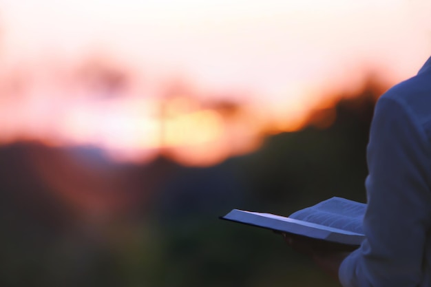 Een christen die leest, mediteert en bidt met het zonsonderganglandschap en de heilige bijbel