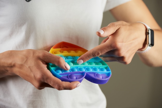 Een close-up foto van een fidget speelgoed "Pop it" in de vorm van een hart in de handen van een meisje. Een jonge vrouw met een slim horloge drukt met haar enkele vinger op de hobbels en ontspant.