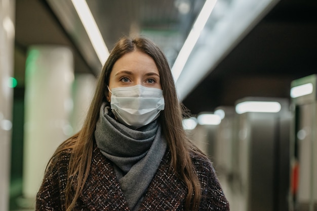 Een close-up foto van een vrouw met een medisch gezichtsmasker om de verspreiding van het coronavirus te voorkomen die op een trein op het metroplatform wacht. Meisje met een masker houdt sociale afstand in de metro.