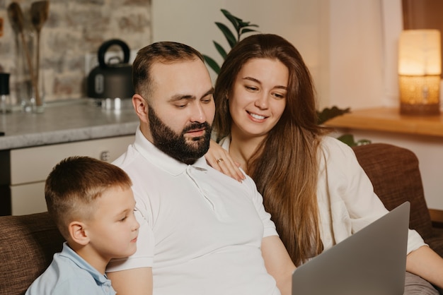 Een close-up foto van vader met een baard die zijn prestaties op het werk op een laptop aan zijn zoon en glimlachende vrouw thuis toont