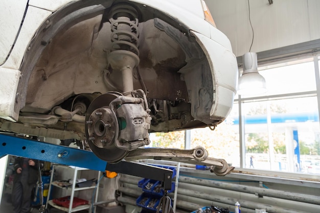 Een close-up op het remsysteem en het chassis van een witte auto met remblokken, schijven, een remklauw op een lift in een industriële dienst voor autoreparatiewerkplaatsen