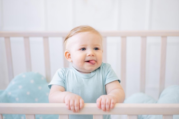 Een close-up portret van een kleine blonde baby een baby met blauwe ogen laat zijn tong zien terwijl hij in een criba zit plaagt een grappig jongetje