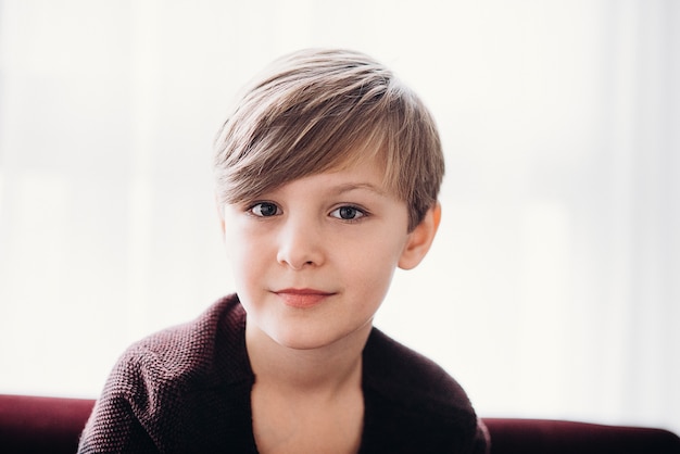 Een close-up portret van een schattige jongen die op een bank zit tegen de zachte focus van het lichte raam