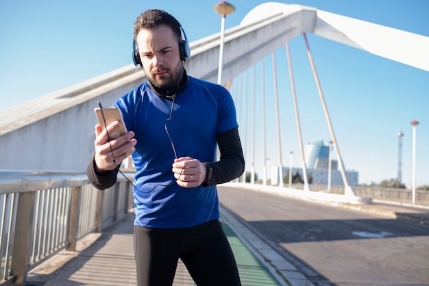 Een close-up shot van een man in blauwe koptelefoon met zijn mobiel tijdens het joggen in de straat