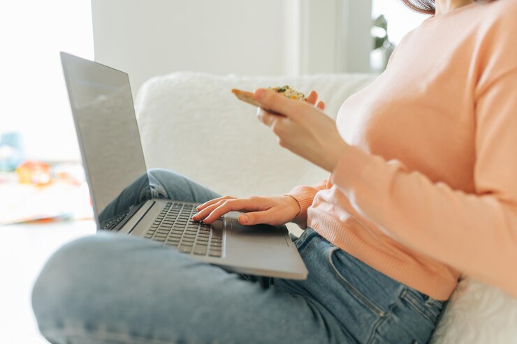 Foto een close-up van de handen van een jonge vrouw die op een laptop tikt terwijl ze thuis werkt en geniet van een stukje pizza die door de hand van een vrouw wordt opgehouden terwijl ze online winkelsites surft