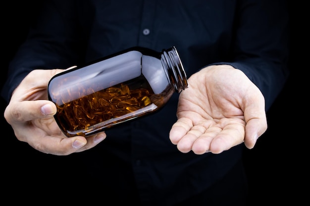 Een close-up van de handen van een man die een pot visoliecapsules vasthoudt, giet capsules op zijn handpalm