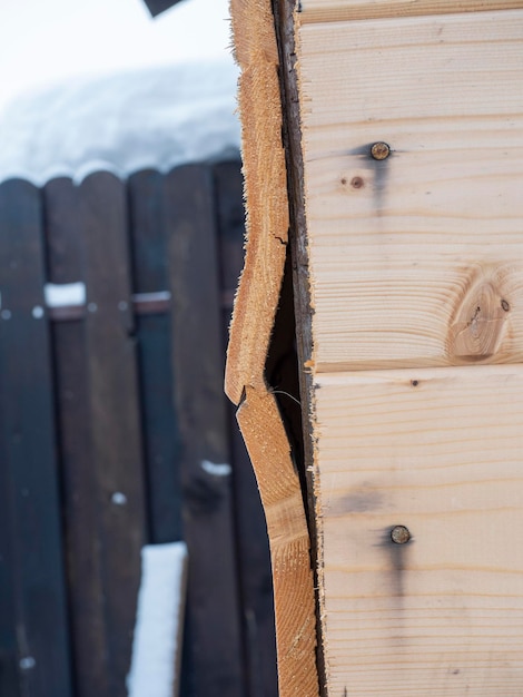 Een close-up van een deel van een houten muur gemaakt van dakspaan van slechte kwaliteit een gat in de muur een gebogen bord het concept van constructie en reparatie van lage kwaliteit