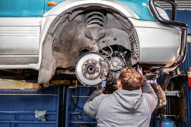 Een close-up van een jonge reparateur in een werkend uniform van auto's repareert een automatische versnellingsbak