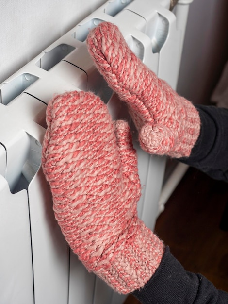 Een close-up van een man legt zijn handen gekleed in roze wanten op een witte batterij Het concept van de winterperiode problemen met centrale verwarming Verwarmingsapparaten in het zijaanzicht van het huis