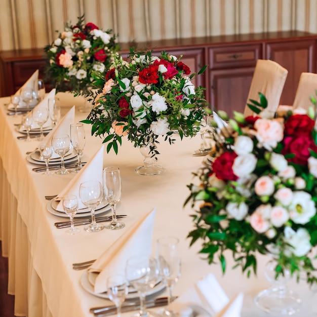 Een close-up van een tafel met een wit tafelkleed waarop bestekborden met servetten en glazen mooie boeketten in transparante vazen