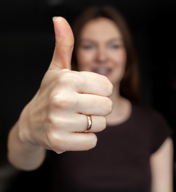 Een close-upbeeld van een jonge vrouw die een thumbsup doet en laat zien op een donkere achtergrond