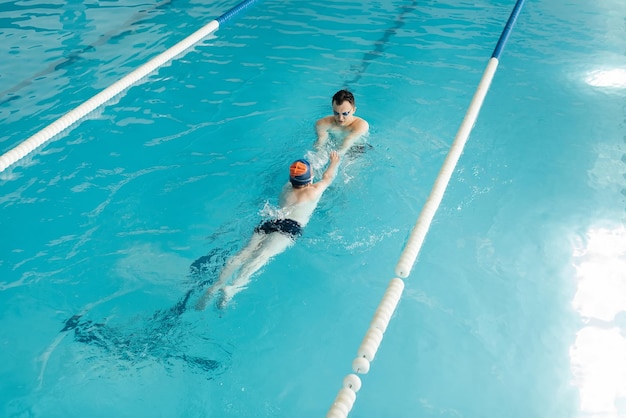 Een coach leert een zevenjarige jongen zwemmen in een modern zwembad Leren zwemmen Ontwikkeling van kindersporten Gezond ouderschap en promotie van kindersport