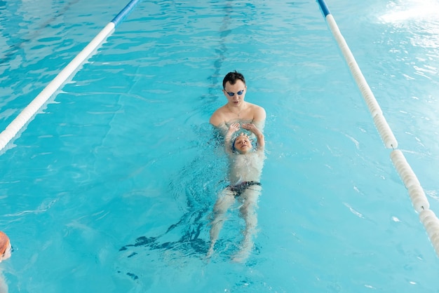 Een coach leert een zevenjarige jongen zwemmen in een modern zwembad Leren zwemmen Ontwikkeling van kindersporten Gezond ouderschap en promotie van kindersporten