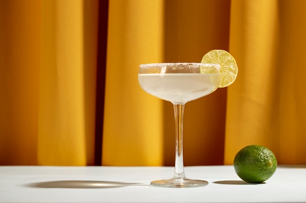 Een cocktail van citroenmargarita met partjes limoen en zout op witte tafel tegen geel gordijn