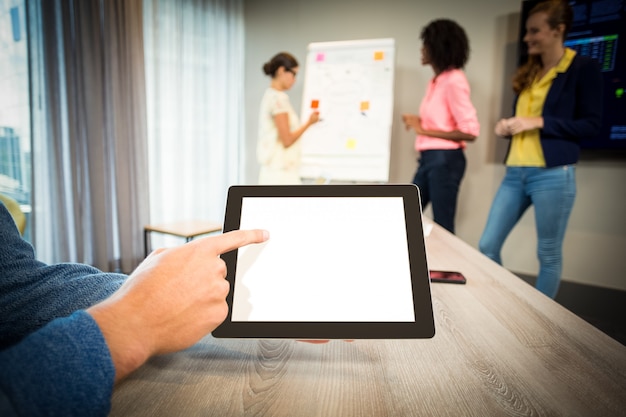 Een collega die digitale tablet gebruikt terwijl collega's stroomschema op whiteboard bespreken