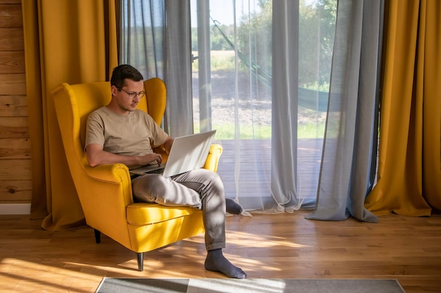 Een comfortabele plek om thuis te werken Een man zit en werkt in een grote gele fauteuil in een zonnig loft-appartement