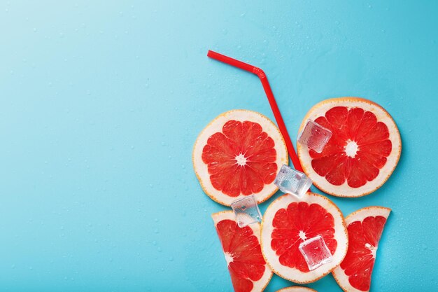 Een compositie van grapefruitschijfjes en ijsblokjes met een rietje op een blauwe achtergrond