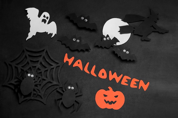 Een compositie van Halloween met papieren vleermuizen, spinnen en geesten met een inscriptie op een zwarte achtergrond