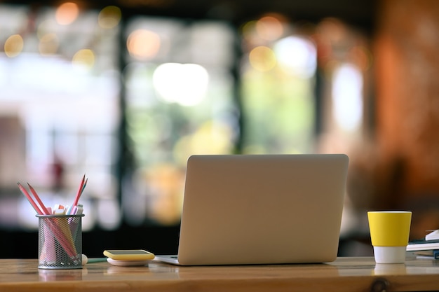 Een computerlaptop, een koffiekop en briefpapier op houten lijst met moderne bureau vage achtergrond.