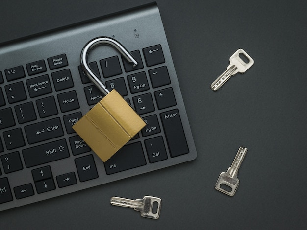 Een computertoetsenbord, een open slot en drie sleutels op een donkergrijze achtergrond. Het concept van computerbeveiliging. Plat leggen.