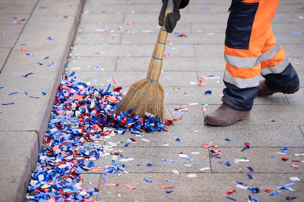 Een conciërge ruimt confetti op met een bezem aan de kant van een stadsstraat na een feestelijke gebeurtenis