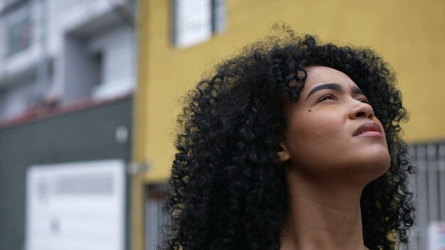 Een contemplatieve zwarte vrouw die buiten staat en naar de lucht in de straat kijkt